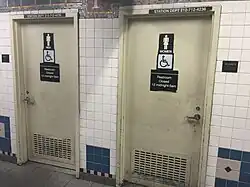 A pair of somewhat decrepit looking metal doors, one labled "MEN", the other labeled "WOMEN", with matching pictograms.  Each has a sign saying "Restroom Closed 12 midnight – 5 am" and a wheelchair pictogram.