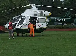 The former helicoper of GNAAS, G-GNAA, shown landed in a field in Darlington. A man in hi-vis clothing is leaning in its opened side door.