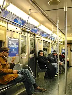 Interior view of a subway car showing the placement of over-window advertising posters.