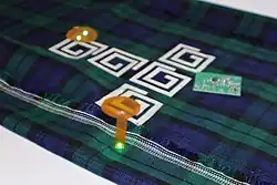 Printed tartan fabric with wireless charging coils, overlaid with multiple illuminated electronic circuit boards