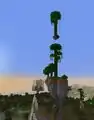 A jungle tree on a tiny floating island above another jungle tree on top of a mountain.