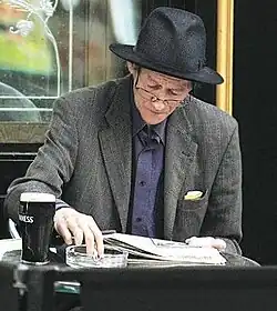 Alex Higgins seated at a table, reading a newspaper