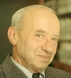 Photo of a man with grey hair wearing a suit and a tie