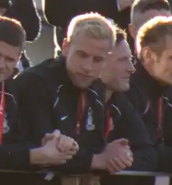 Blond Andrew Davies, leaning on a railing in a crowd