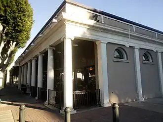 Single-story building with white columns and classical architecture along a street