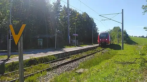 Red train arrives at single-tracked side platform with small wooden shelter