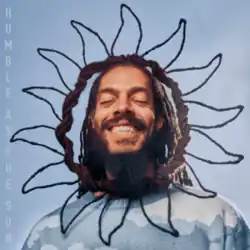 A man with a long beard and hair smiling with eyes closed and wearing a circle wire frame in the shape of the sun around his head.