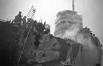 large holes in side of the ship. A ladder leads to the dock. There is also evidence of a fire.