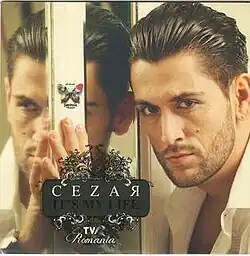Cezar looking at the camera standing next to a mirror which reflects his face.
