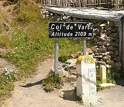 Black sign on the top of the pass, with a crumbling brick wall behind.