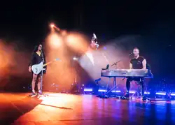 Martin playing the piano as a woman beside him performs with a microphone and guitar