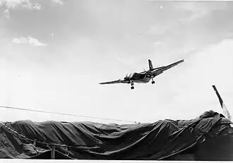 Large airplane descending over tarpaulin-covered area