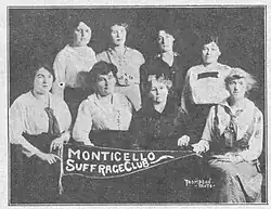 A group of eight white women in 1916, posed together with a banner that reads "Monticello Suffrage Club".