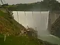 Englebright Dam during spring floods. Water is spilling over the dam's crest. Narrows II Powerhouse is visible at the base of the dam.