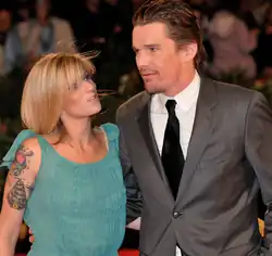 A caucasian woman has blonde hair and wears a light blue dress. The caucasian man has dark slick hair, and a short beard and mustache. He is wearing a gray suit and black tie with a white shirt.