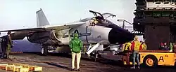 An F-111B on the deck of an aircraft carrier being towed.