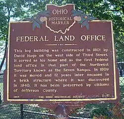 historical marker saying Federal Land Office This log building was constructed in 1801 by David Hoge on the west side of Third Street. It served as his home and as the first Federal land office in that part of the Northwest Territory known as the Seven Ranges. In 1809 it was moved, and twelve years later encased in a brick structure where it was discovered in 1940. It has been preserved by the citizens of Jefferson County.
