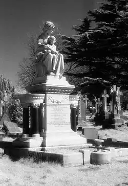 A grayscale photo of a large monument topped with a statue of a woman holding a child.