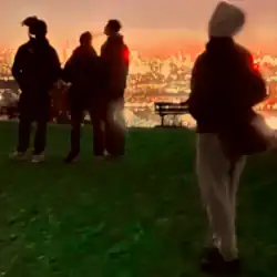 Four people stand on a grassy lookout overlooking a city illuminated by lights
