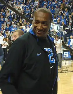A man, wearing a black jacket and black T-shirt, is walking onto the basketball court.