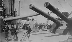 The crowded midships area of HMS Indomitable dominated by the masses of the 12-inch guns of 'P' and 'Q' turrets, each of which is trained across the deck
