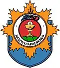 A blue crest with a white circle surrounded by a jagged orange shape. In the circle is another red circle with fruits on top of it. Inside the red circle is three green hills with a cross and a chalice on it.