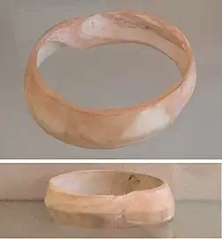Indus bracelet, front and back, made of Pleuroploca trapezium or Turbinella pyrum imported to Susa in 2400–2100 BC. Found in the tell of the Susa acropolis. Louvre Museum, reference Sb 14473.[70] This type of bracelet was manufactured in Mohenjo-daro, Lothal and Balakot.[71] The back is engraved with an oblong chevron design which is typical of shell bangles of the Indus Civilization.[72]