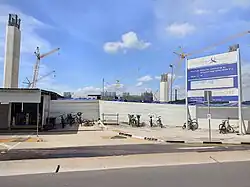 A construction area with several tall concrete columns and multiple tower cranes at work in the background