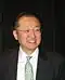 Photograph of Jim Yong Kim in a suit and patterned green tie, wearing glasses and smiling.