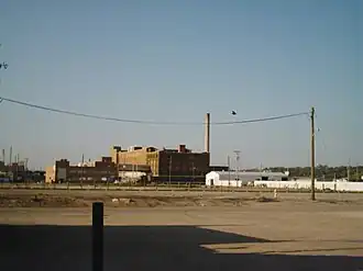 Fuzzy photo of five- or six-story brick building with a single tall smokestack