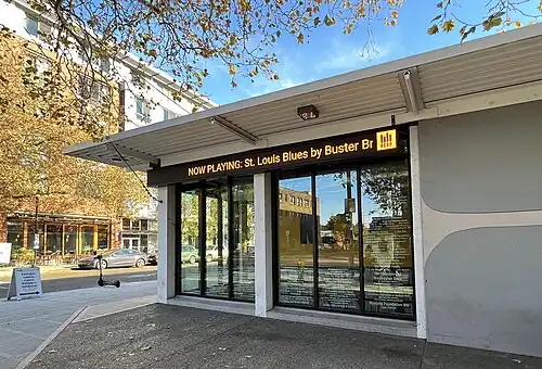 The side of a building with long LED sign near the roof, which includes the yellow KEXP logo and the song title