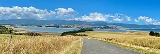 A large lake surrounded by farmland on a sunny day, with a road running towards the lake.