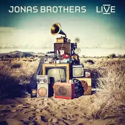 A pile of old radios and televisions with a gramophone on top, in the middle of the desert.