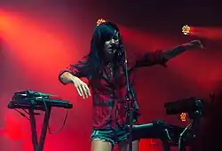 A woman surrounded by keyboards, singing into a microphone.
