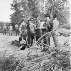 Asian men wearing blindfolds are standing while white soldiers stand behind them.