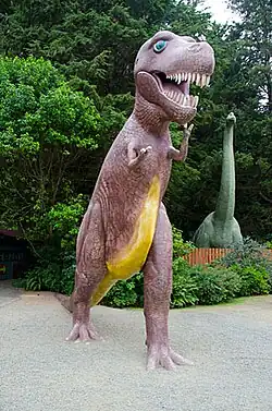 brightly colored sculpture of a carnivorous dinosaur, with a herbivore dinosaur in the background