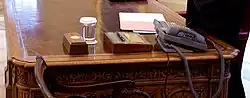 a close-up view of the resolute desk showing the Presidential call button and the HMS Gannet pen holder.