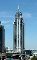 Distant ground-level view of a 40-story building with a square cross section; the tower has a mostly glass facade and has a light blue color. On the roof there is large, latticework structure that tapers into a spire.