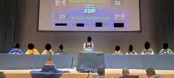 Eight players, four on each team, competing in a trivia tournament with the host in the middle, with their faces censored