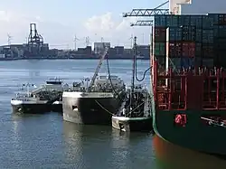 A container ship lying in port, being refuelled by oil tankers
