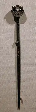 a dark hatpin with celtic designs on it, pinned to a display board