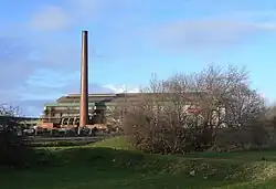 A long building with a tall cylindrical chimney on the left-hand side