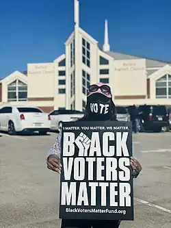 Woman holding a black sign with white lettering that reads "Black Voters Matter"