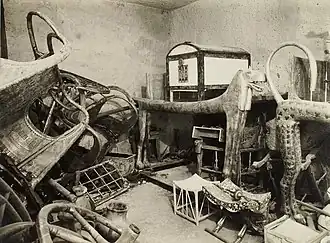 A bare-walled room containing various stacked and jumbled wooden objects