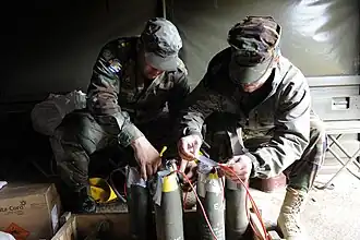 A group of 105&nbsp;mm artillery shells with plastic explosive stuffed into their fuze pockets to act as booster charges. Each of the five shells has been linked together with red detcord to make them detonate simultaneously. To turn this assembly into a booby trap, the final step would be to connect an M142 firing device to the detcord and hide everything under some form of cover e.g. newspapers or a bed-sheet.
