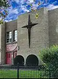 A tan brick building with a wood-style north star cross