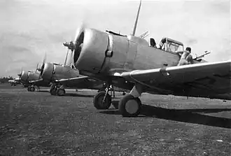 Row of single-engined military monoplanes on airfield, propellers spinning