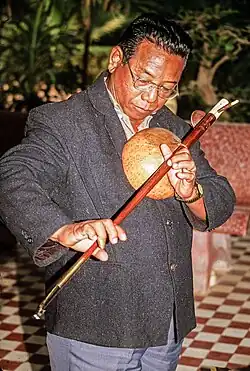 Cambodia, 21st century. Yoeun Mek plays a Kse diev heterochord stick zither, which uses a gourd for a resonator.