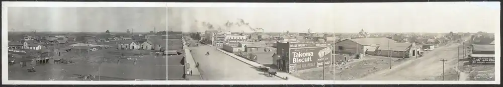 A panoramic view showing wooden houses and businesses, many along two main dirt roads that meet at a corner